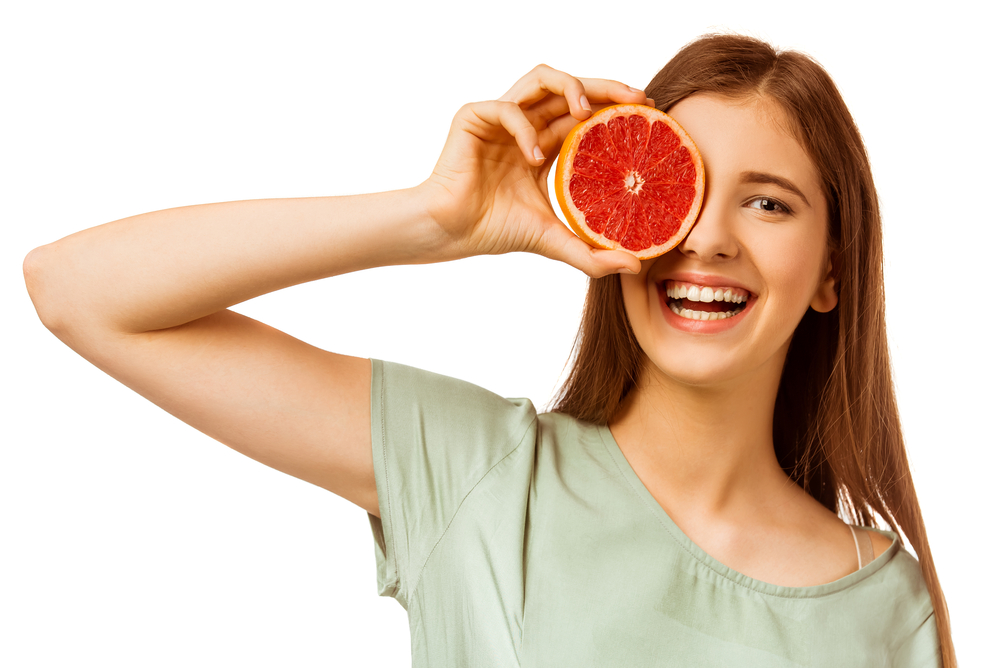 Young woman holding grapefruit in front of her eye