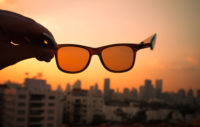 Hand Holding Sunglasses In Front Of Sunset